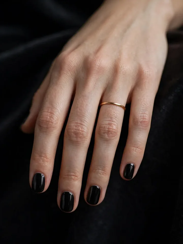 Short round black wedding guest nails worn with a gold wedding band