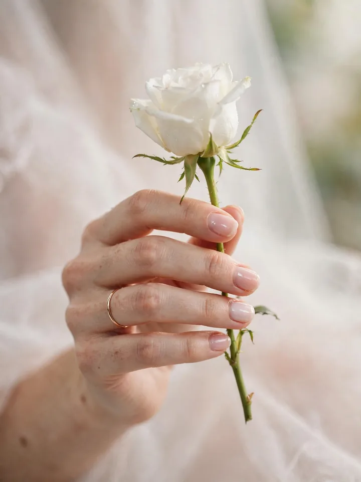 Sheer blush pink short wedding nails for the bride holding a white rose